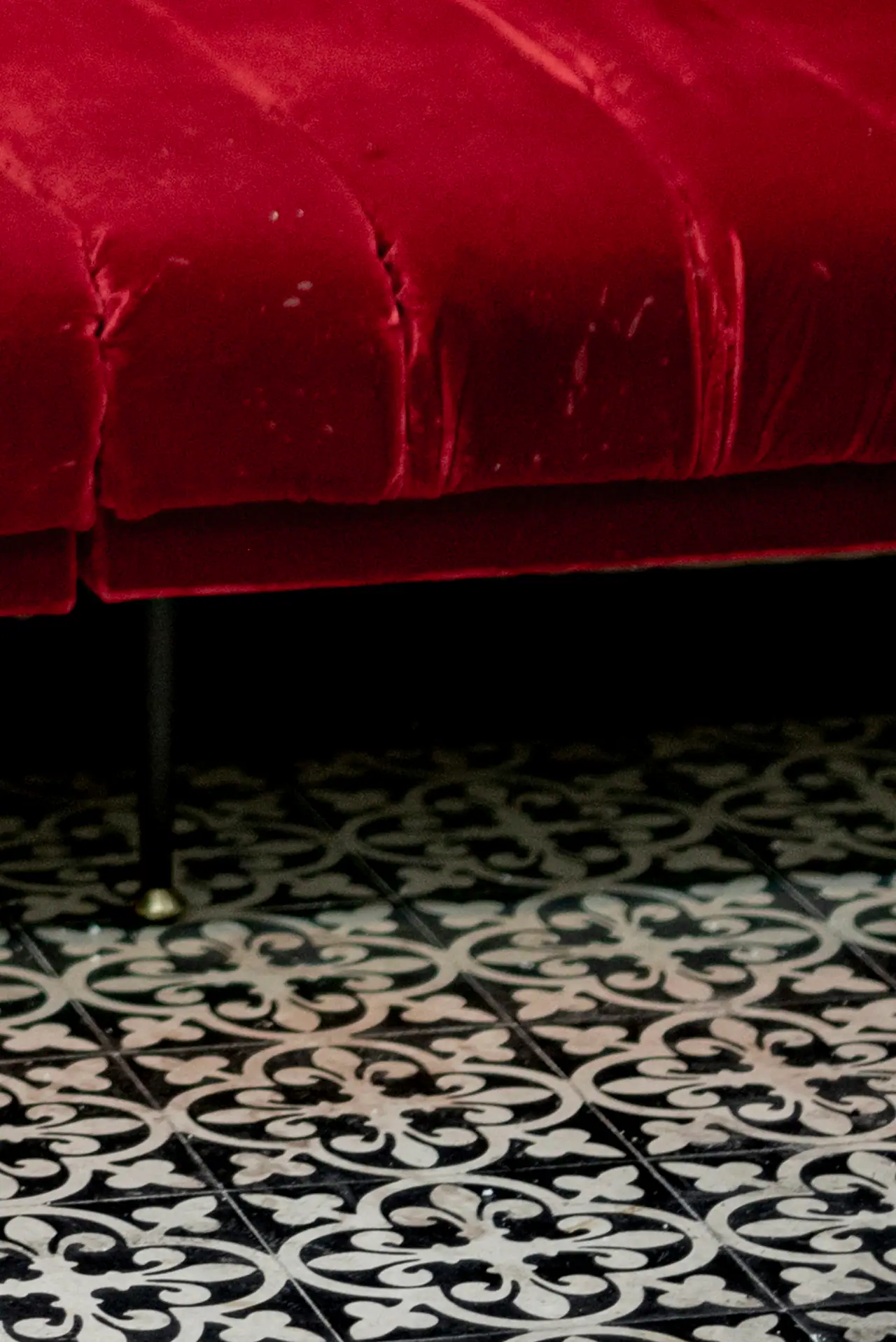 A deep red velvet banquette above a black-and-white patterned tile floor, in a dimly lit room