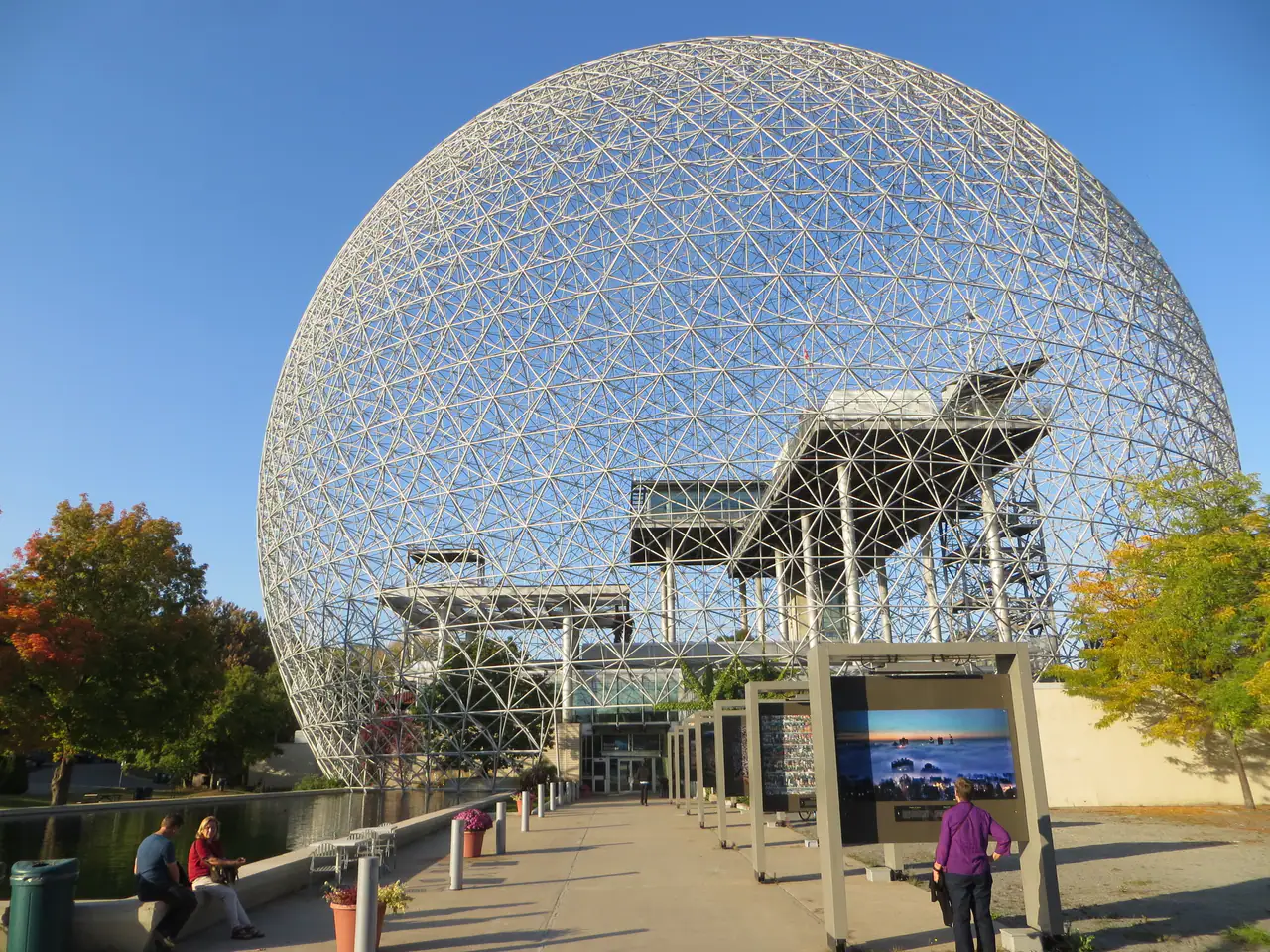 Buckminster Fuller's geodesic dome of the Biosphère on Île Sainte-Hélène, seen from the entrance path with autumn trees at left and a reflecting pool