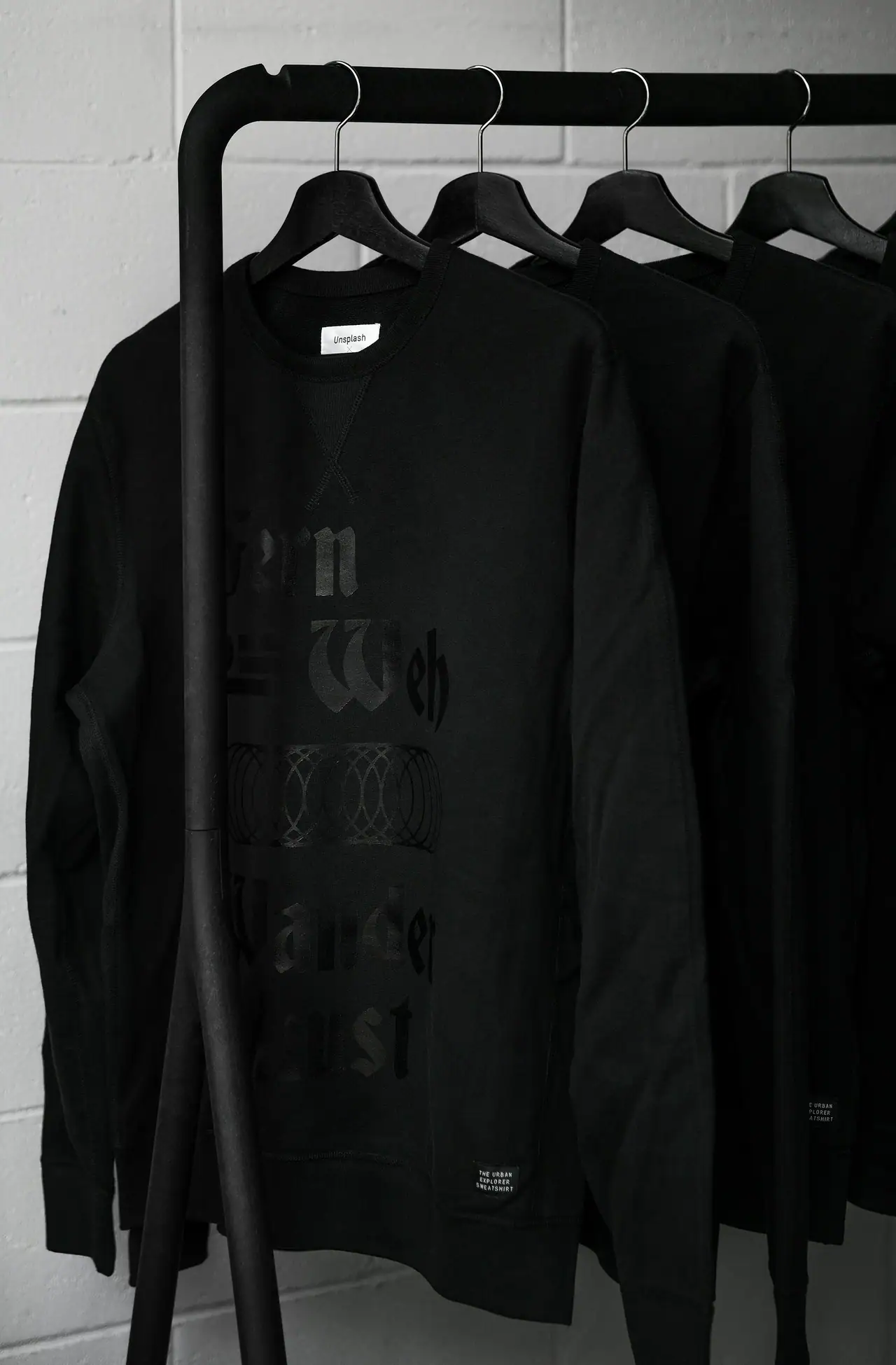 Black graphic crewneck sweatshirts hanging from a black metal rail against a white painted brick wall