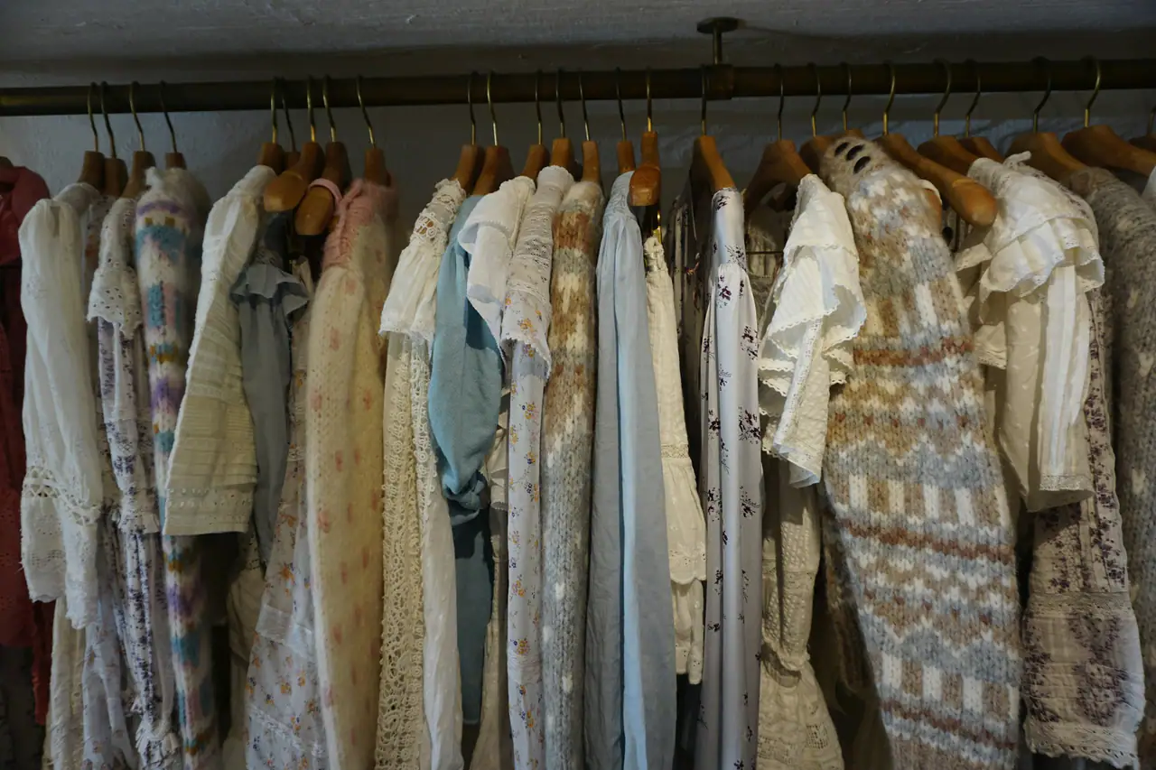 A rail of vintage lace blouses and patterned knitwear on wooden hangers, in soft light