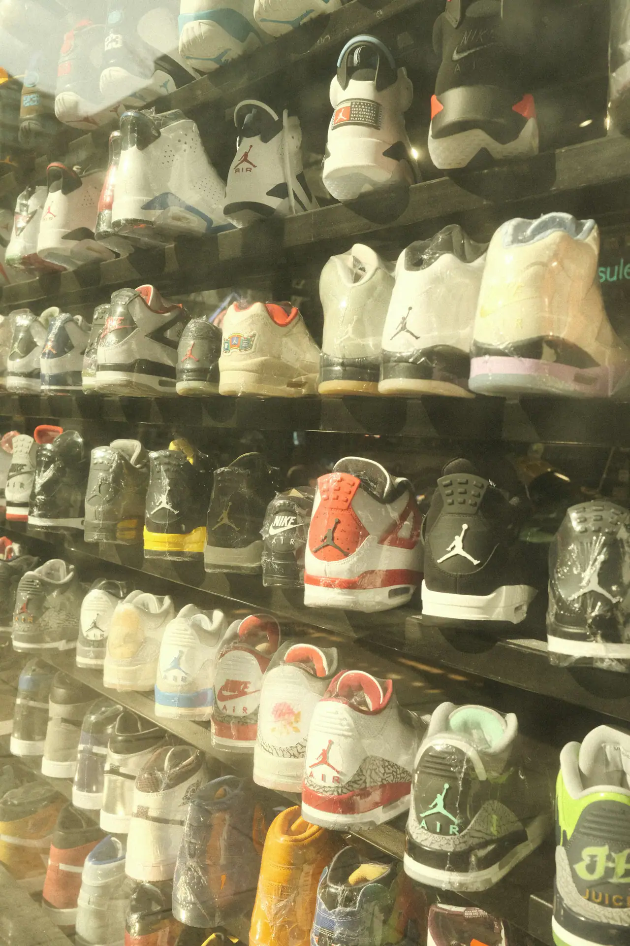 Rows of Jordan and Nike sneakers lined up on dark shelves behind glass, in warm light