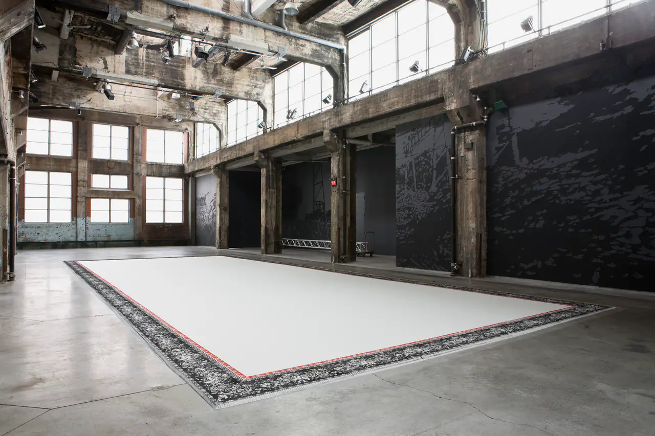 The main hall of the Fonderie Darling, a former metalworks foundry, with raw concrete columns, tall industrial windows and a large pale carpet installation on the floor