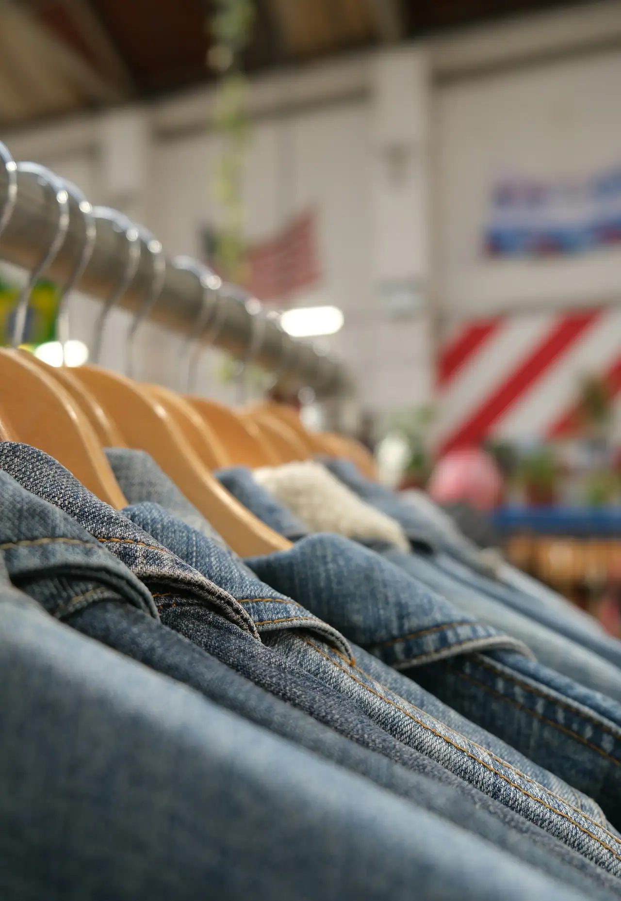 A close row of worn blue denim jackets on wooden hangers along a metal rail in a vintage clothing shop