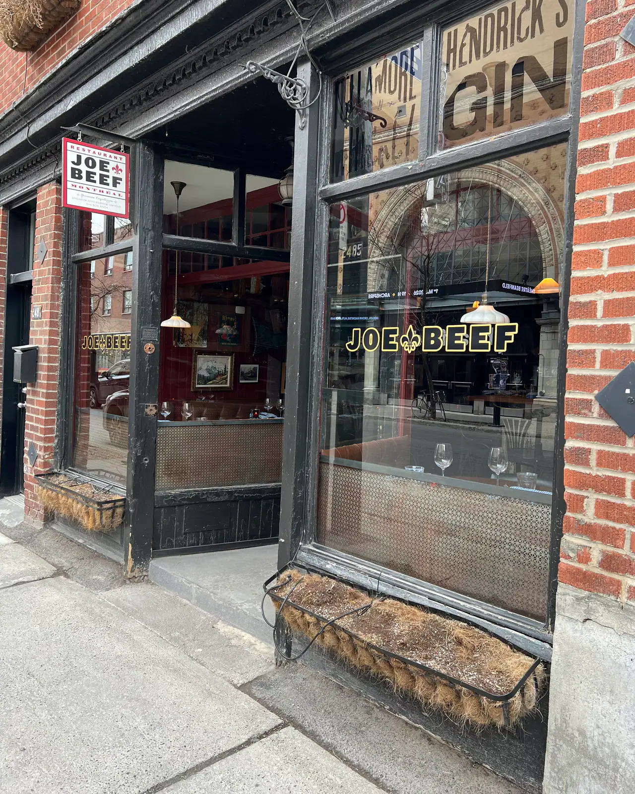 Joe Beef's black-framed brick storefront on Notre-Dame Ouest, gold Joe Beef lettering in the window and wine glasses set on the tables inside