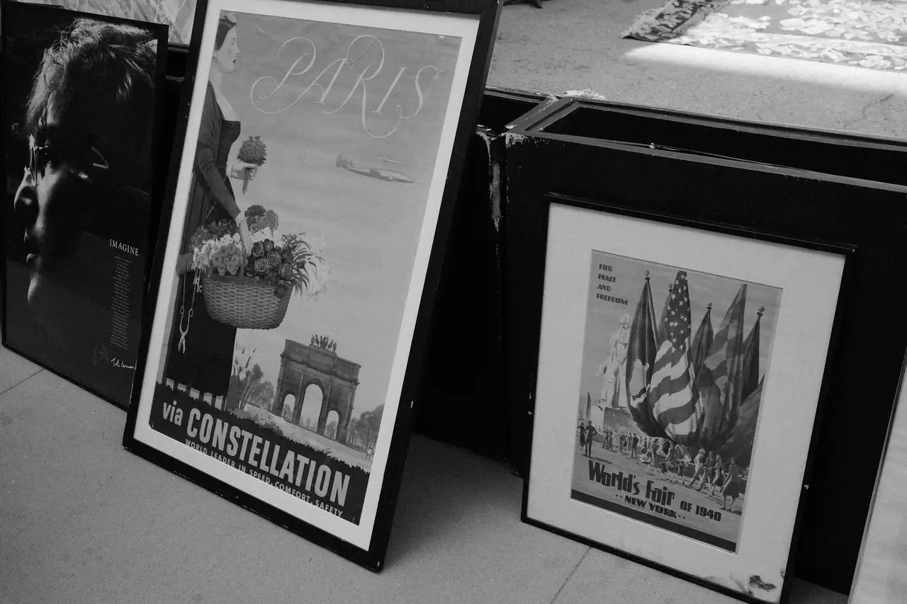 Framed vintage travel posters leaning against each other in black and white, including a Paris 'via Constellation' airline poster and a 1940 New York World's Fair poster