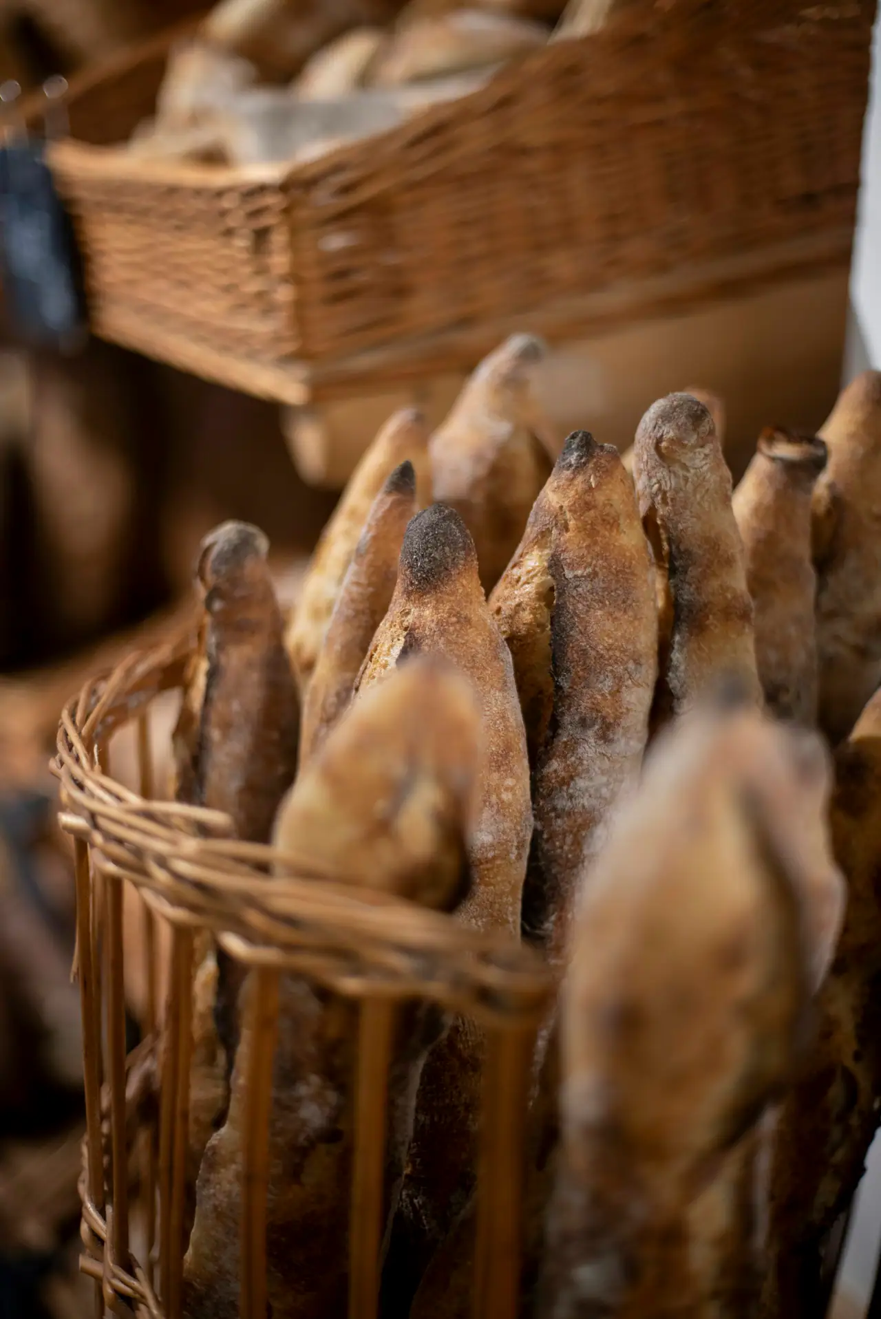 Close-up of crusty sourdough baguettes standing in a wicker basket, with more baskets of bread softly blurred behind