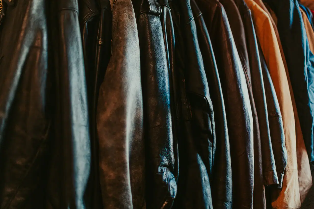A tightly packed rail of worn leather jackets in black, brown and tan, hanging side by side in warm low light