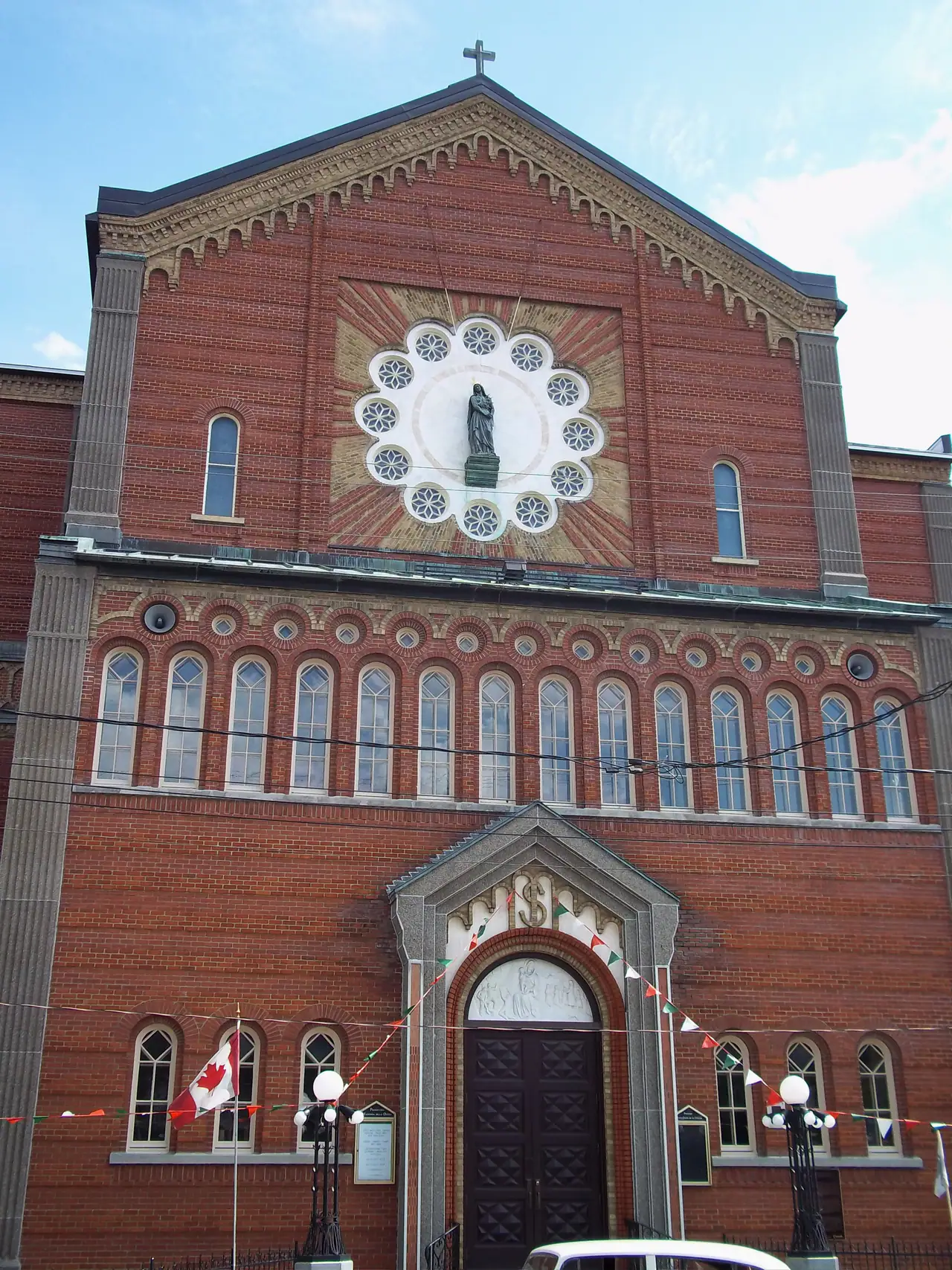 Red-brick facade of the Madonna della Difesa church in Montréal's Little Italy, with a white rose window, arched windows and small Italian flag bunting above the door