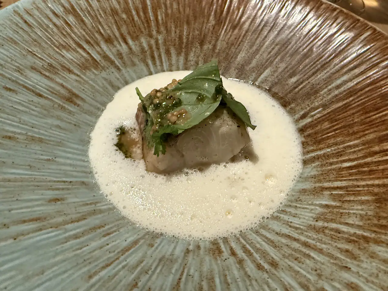Walleye with leek and mustard seeds under a basil leaf, in a pale foam, served in a speckled blue-grey bowl at Mastard