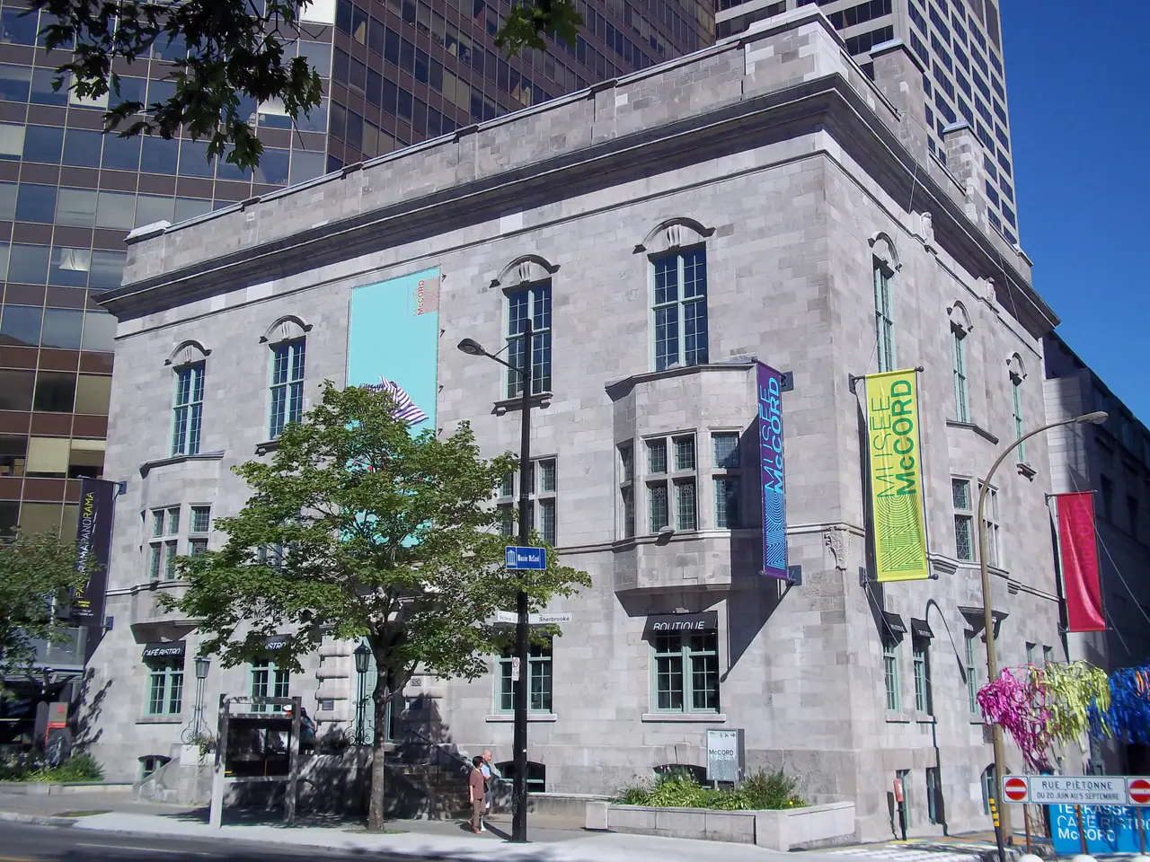The grey limestone corner facade of the McCord Stewart Museum on Sherbrooke Street, with bay windows and Musée McCord banners