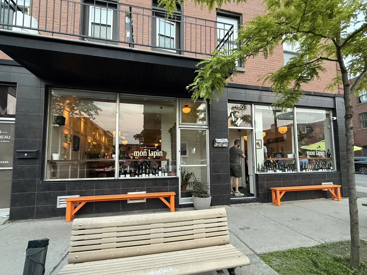 Mon Lapin's black-tiled corner storefront on Rue Saint-Zotique at dusk, wine bottles lined up in the windows and orange benches out front