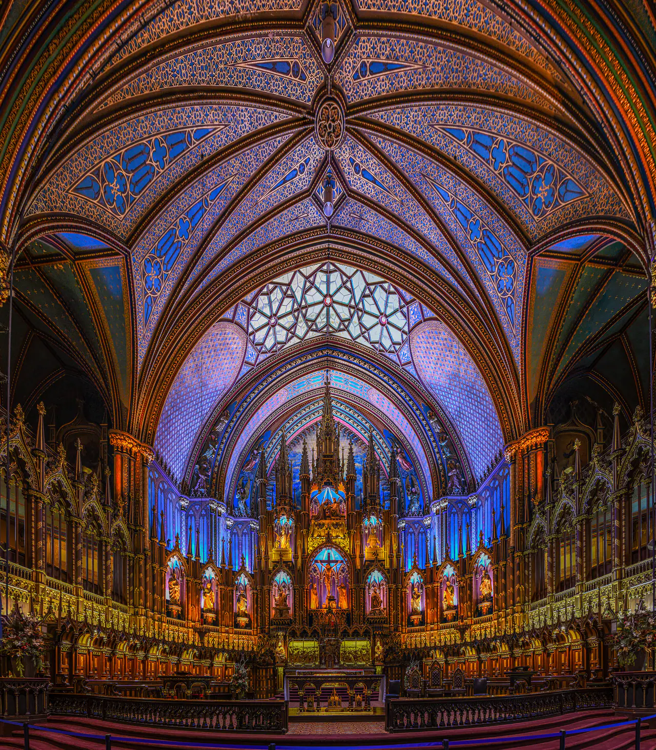 Looking up the chancel of Notre-Dame Basilica in Old Montréal: a ribbed Gothic Revival vault painted in deep blue, violet and gold rises over the carved wooden altarpiece and choir stalls.