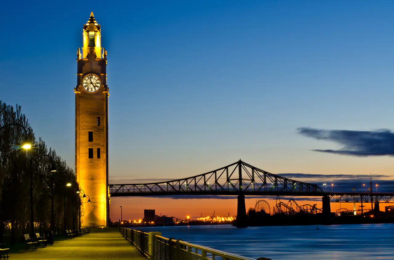 The illuminated Clock Tower in Montréal's Old Port at dawn, with the Jacques-Cartier Bridge and the river beyond