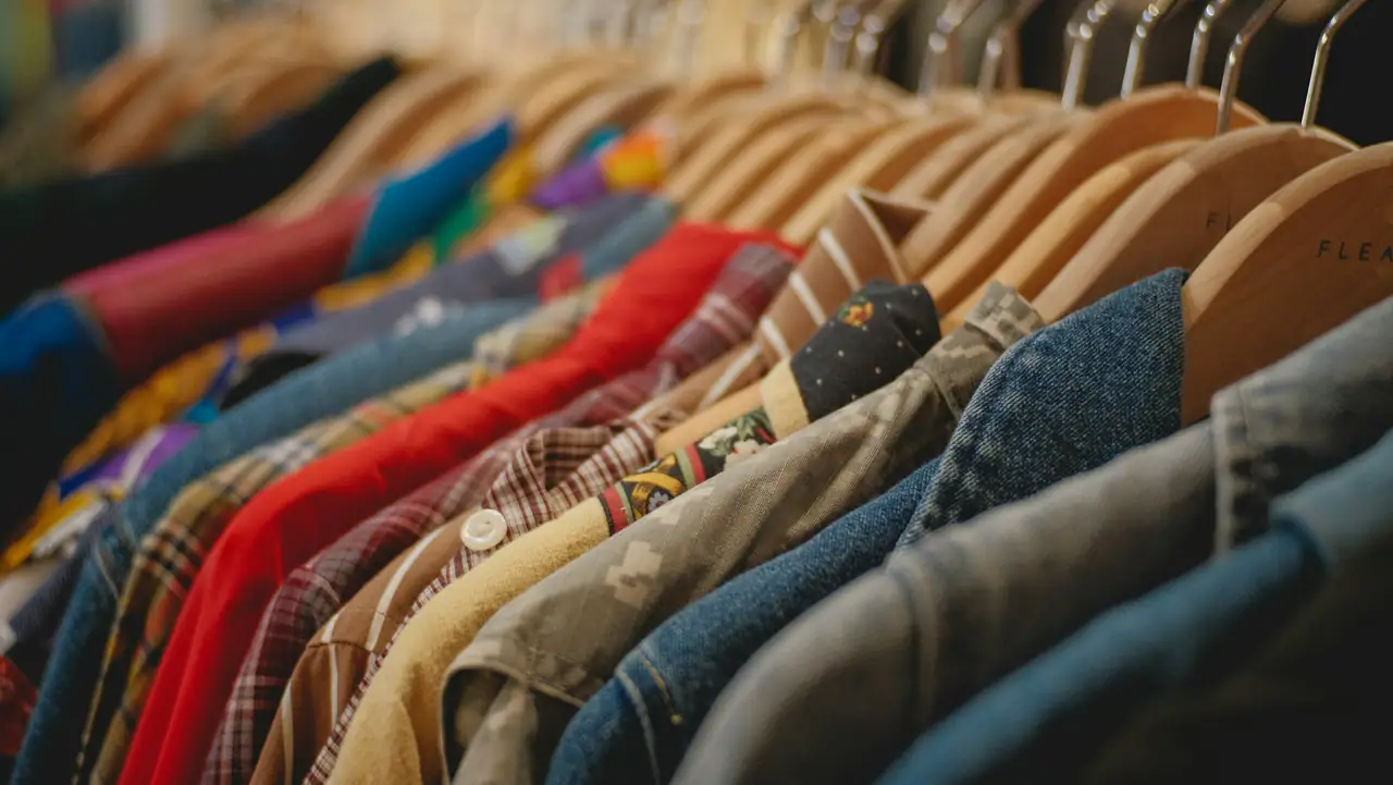Close view of wooden hangers holding denim jackets, plaid shirts and a red top on a vintage clothing rail