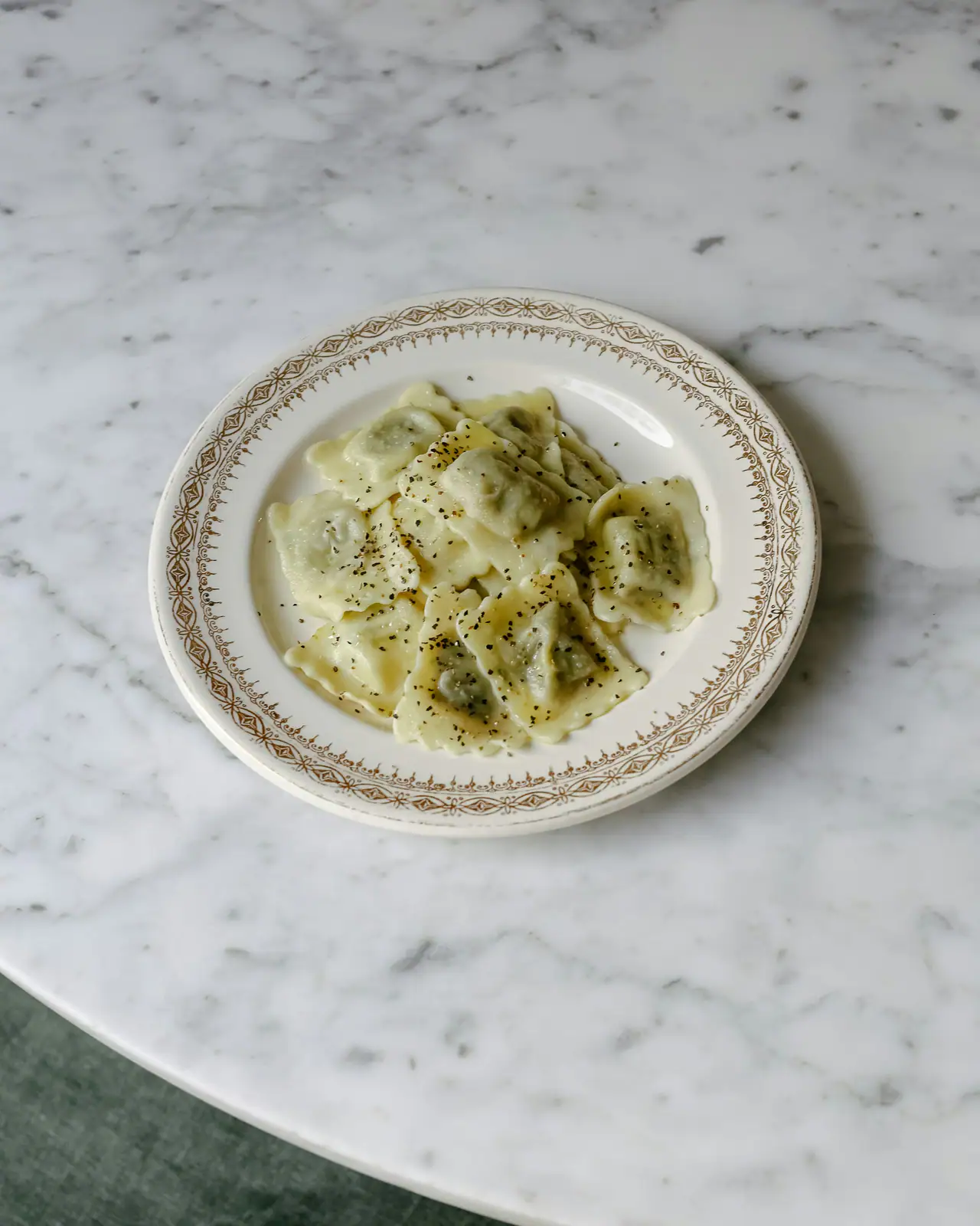 Hand-made filled ravioli with black pepper on a vintage patterned plate, set on a white marble table