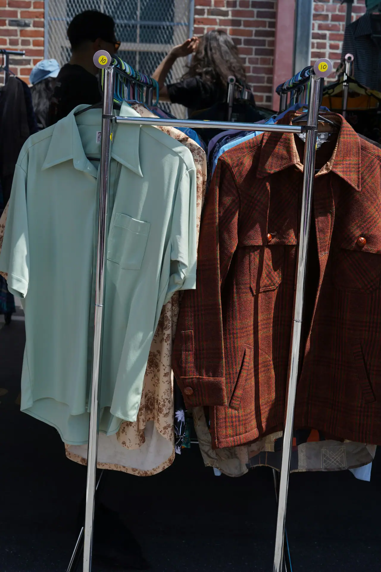 Vintage shirts and a rust plaid wool shirt-jacket with wooden buttons on a chrome clothing rack in front of a brick wall