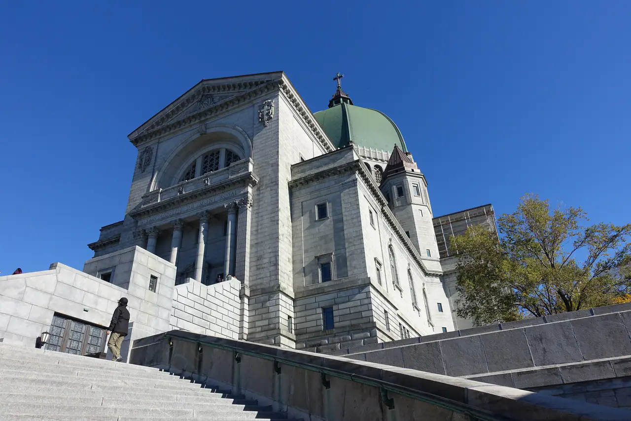 The grey stone facade and green copper dome of Saint Joseph's Oratory seen from the granite steps below, under a clear autumn sky