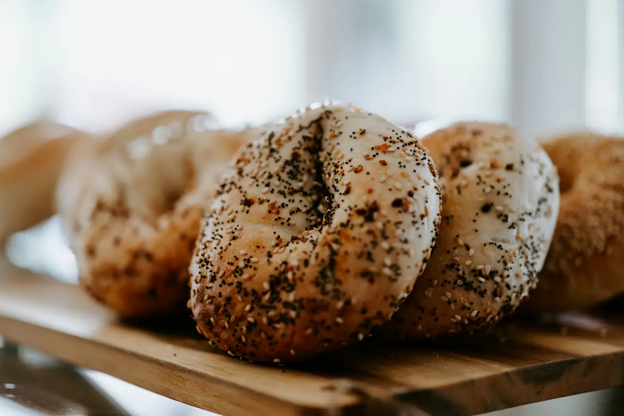 Seeded bagels resting on a wooden board, soft window light behind
