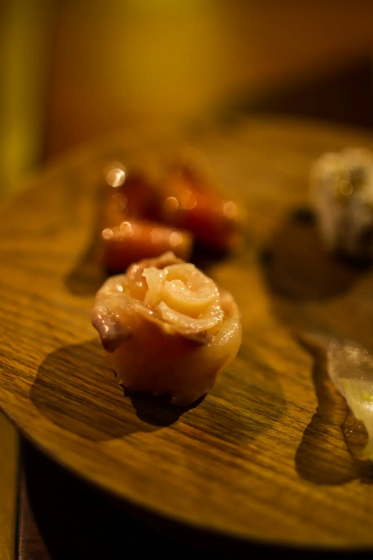 A single rosette of sliced raw fish on a round wooden plate, lit in warm amber low light with soft blurred background